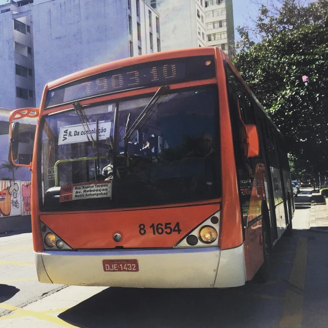 an orange bus is going down the road in the city