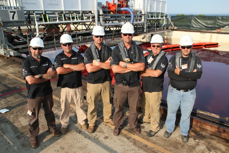 four men in hardhats stand in front of a body of water