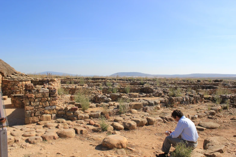 a woman kneeling down near a ruin with trees and rocks