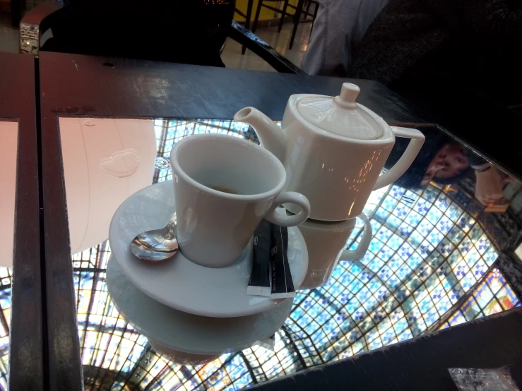 two white cups sitting on a table with a glass