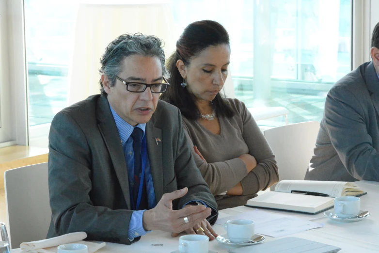 a man in business attire standing next to a woman while sitting down