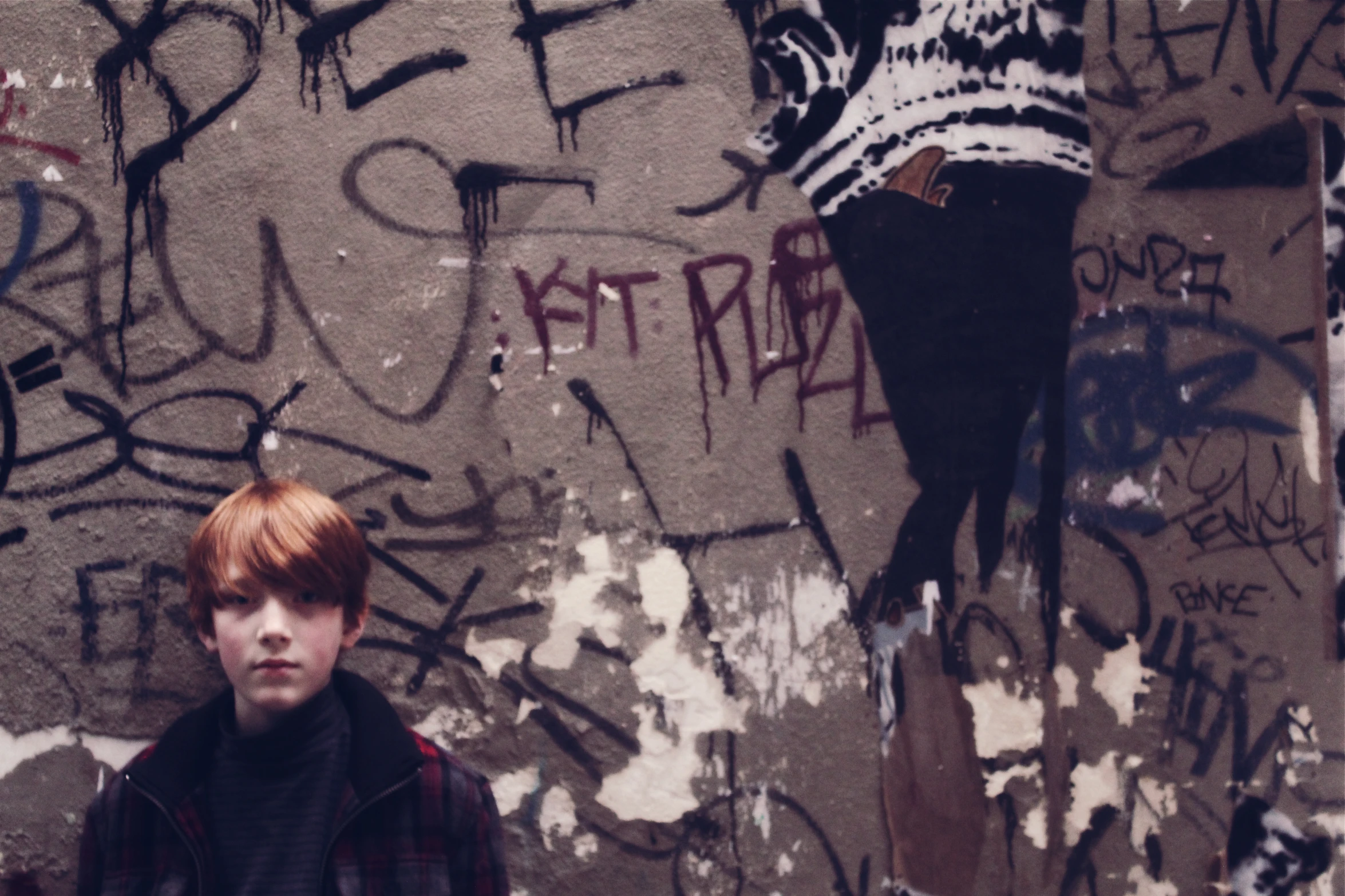 a boy stands near a wall covered in graffiti