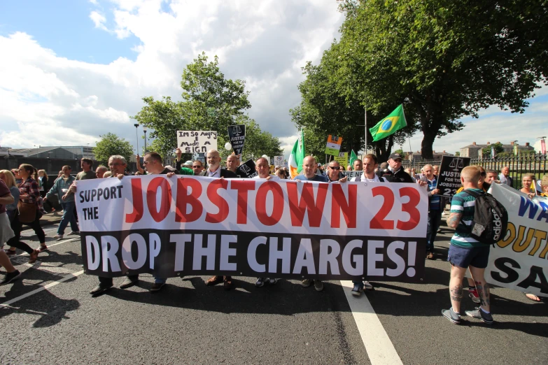 protesters march in a rally carrying signs that read, jobstown 223 drop the chargers