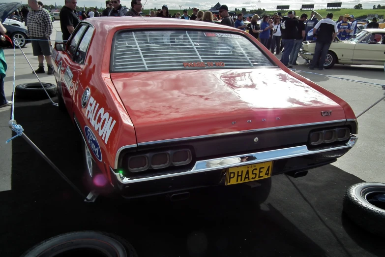 a red classic car parked in front of a crowd