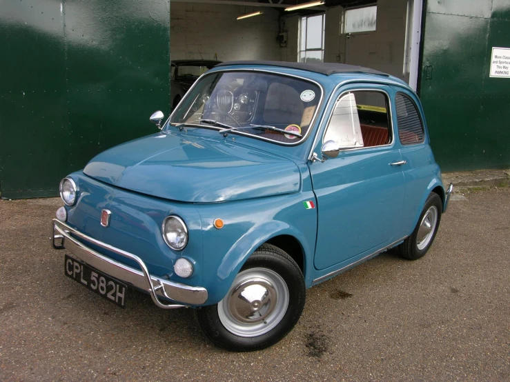 a classic blue car sitting in front of a green garage