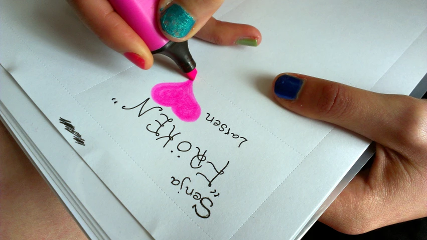 a person with colorful fingernails writing on a note