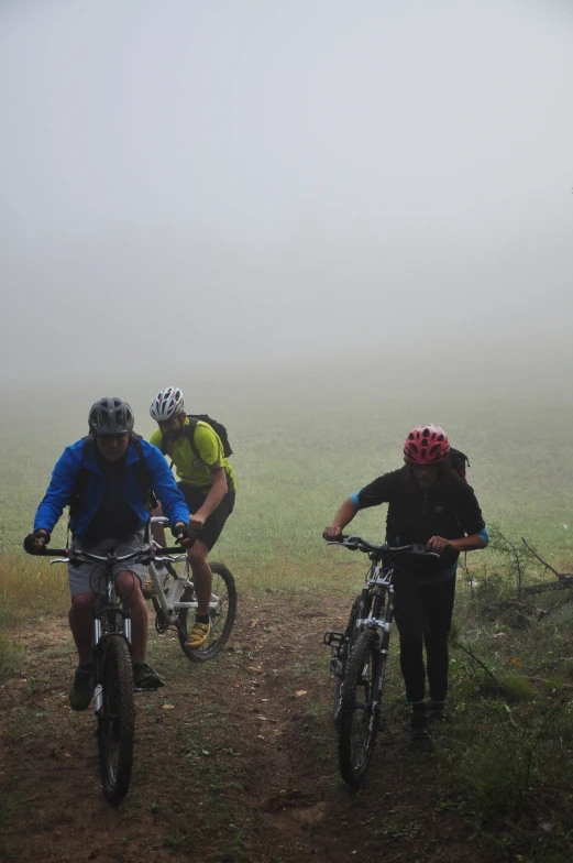 three men standing on bikes and riding the trail on a foggy day