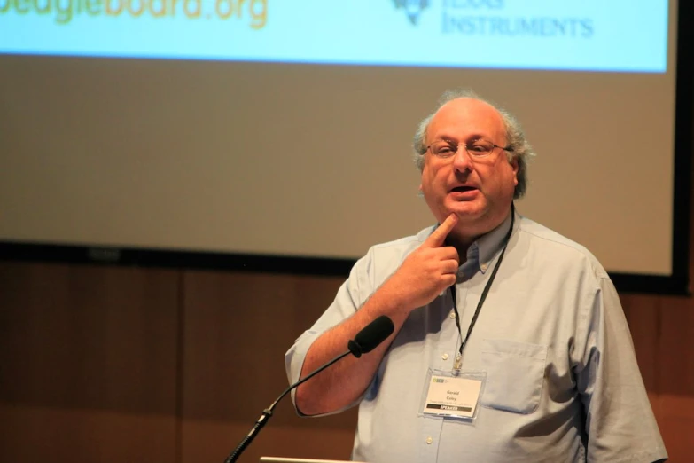 a man standing in front of a projection screen at a podium holding a microphone