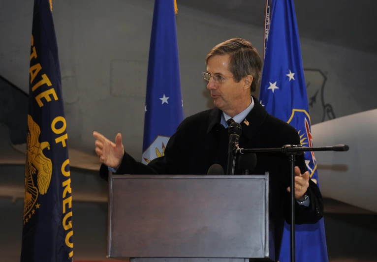 a man at a podium giving a speech in front of flags