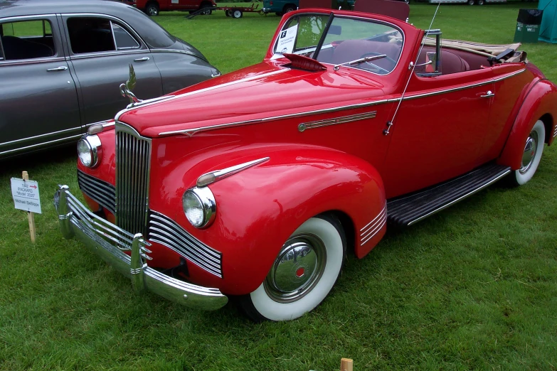 an old red car is parked on some grass