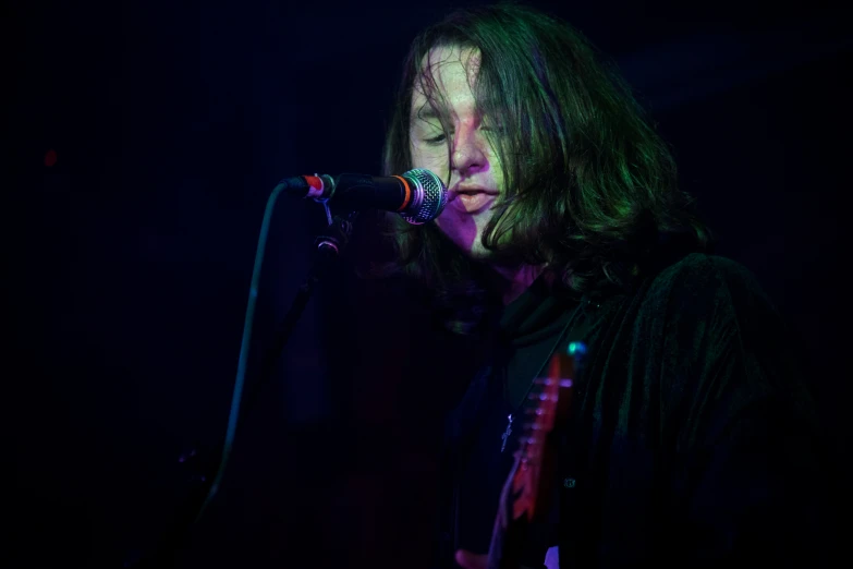 a man with long hair playing the guitar and singing into a microphone