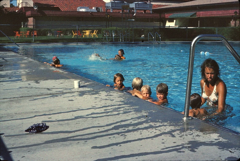 children swimming in a swimming pool with their mom standing by