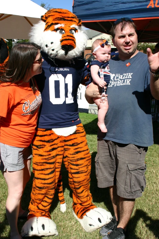 people stand in front of the auburn football mascot and a baby