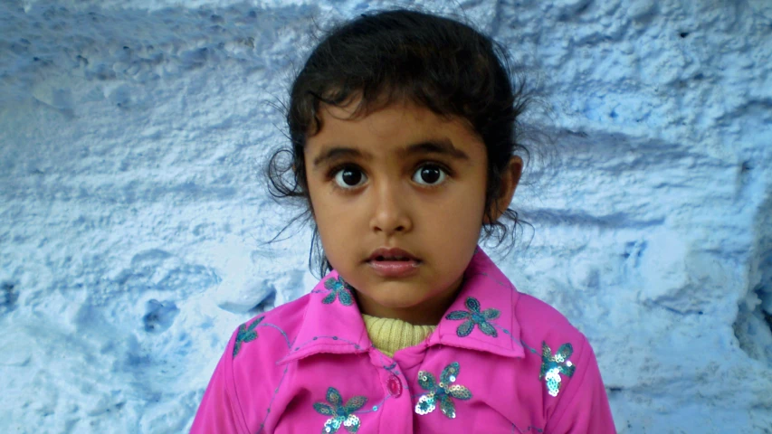 a small child with a pink shirt stands near a blue wall