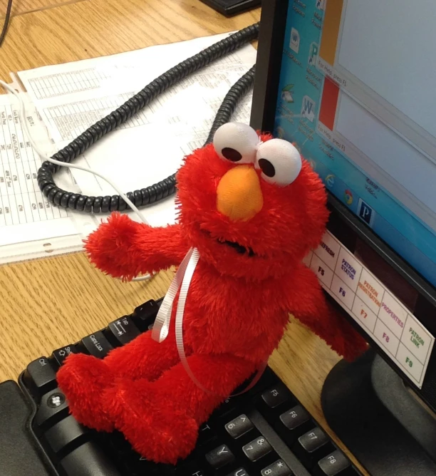 red stuffed elmo sitting on a computer keyboard