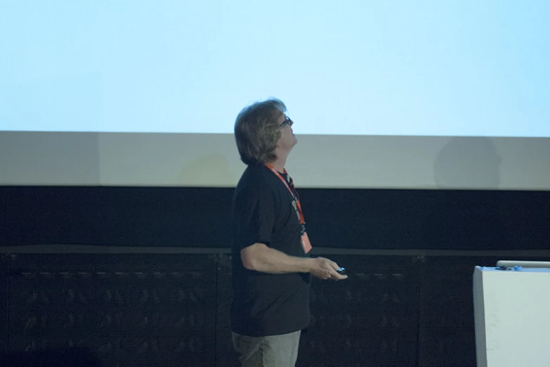 a man in black shirt standing next to a projector screen
