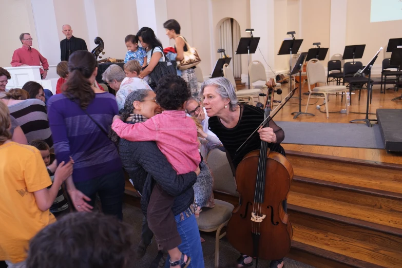 a woman holding a child with a violin in front of a crowd