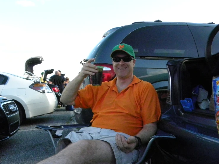 a man with a cup sits in a chair next to his trunk