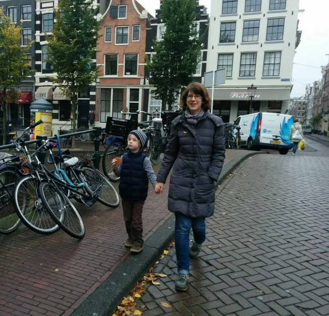 woman and little boy are walking down a cobblestone walkway between two buildings