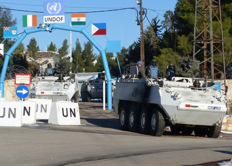 several armored vehicles are parked under an arched blue sign