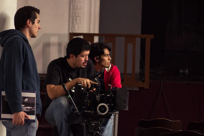 three young men watching one man filming a video