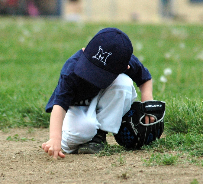 a little boy is kneeling in the grass with his head in a baseball glove