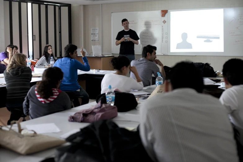 people sitting in chairs around tables while a man giving a presentation to them