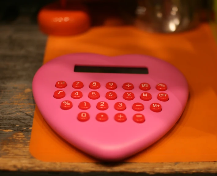 a pink heart shaped calculator sitting on top of a piece of orange paper