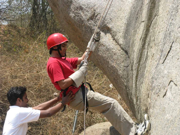 two men climbing up rocks with one trying to climb