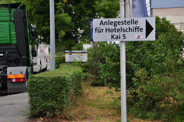 a street sign near a bush, with a truck in the background