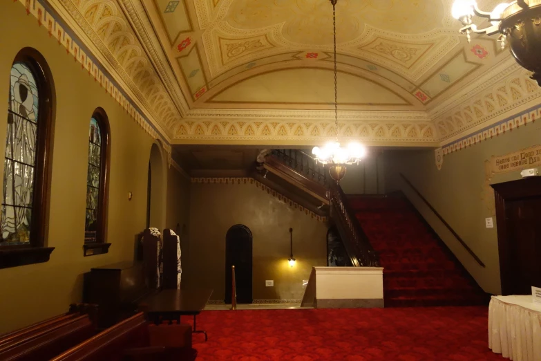 an old mansion staircase with red carpet and a chandelier