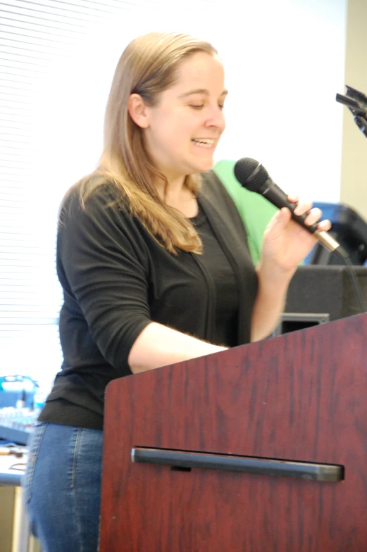 a woman talking into a microphone standing in front of a lecterte