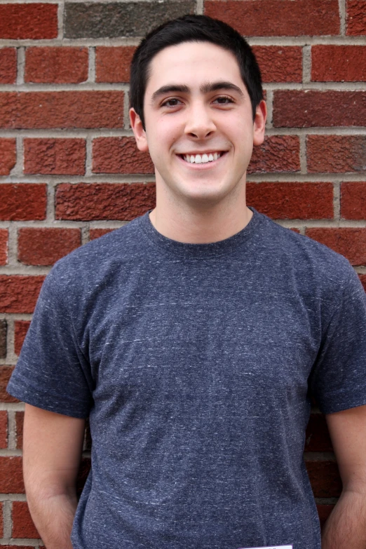 a young man posing for a picture in front of a brick wall