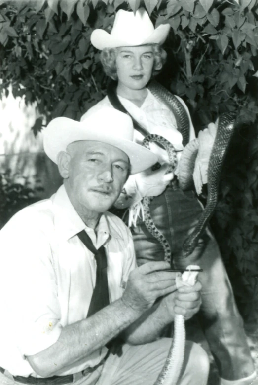 man and woman in western clothing holding up a small rope snake