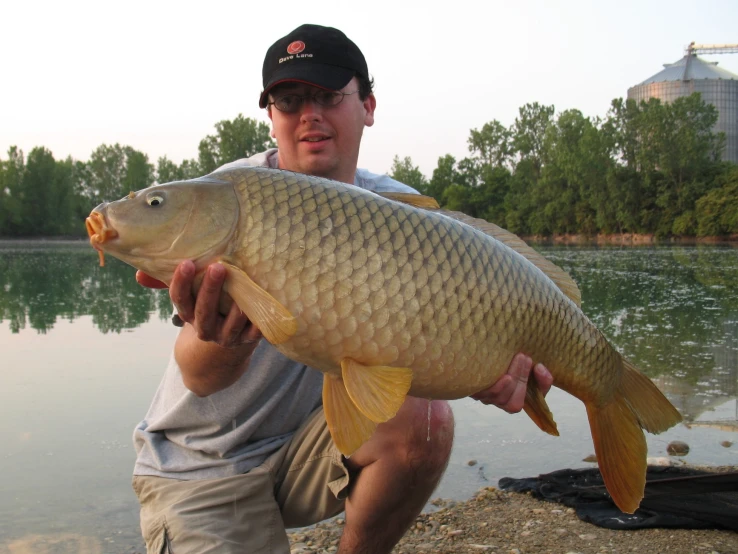 a man holding up a large fish in front of water