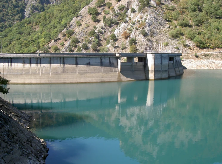 a concrete structure by the water with a view of trees and mountains