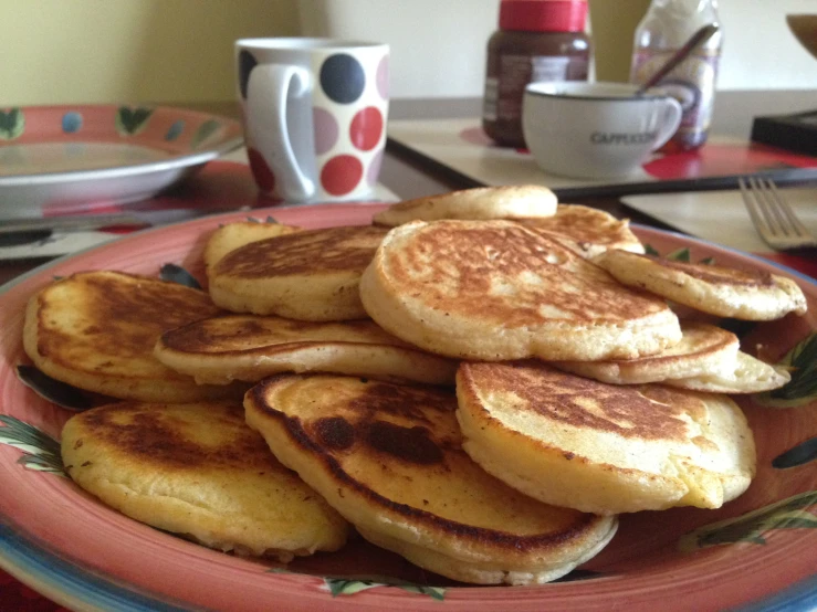 pancakes on an orange plate, with coffee cups and vases in the background