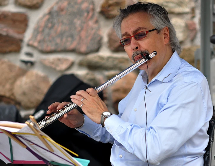 an elderly man wearing glasses plays the recorder in his band