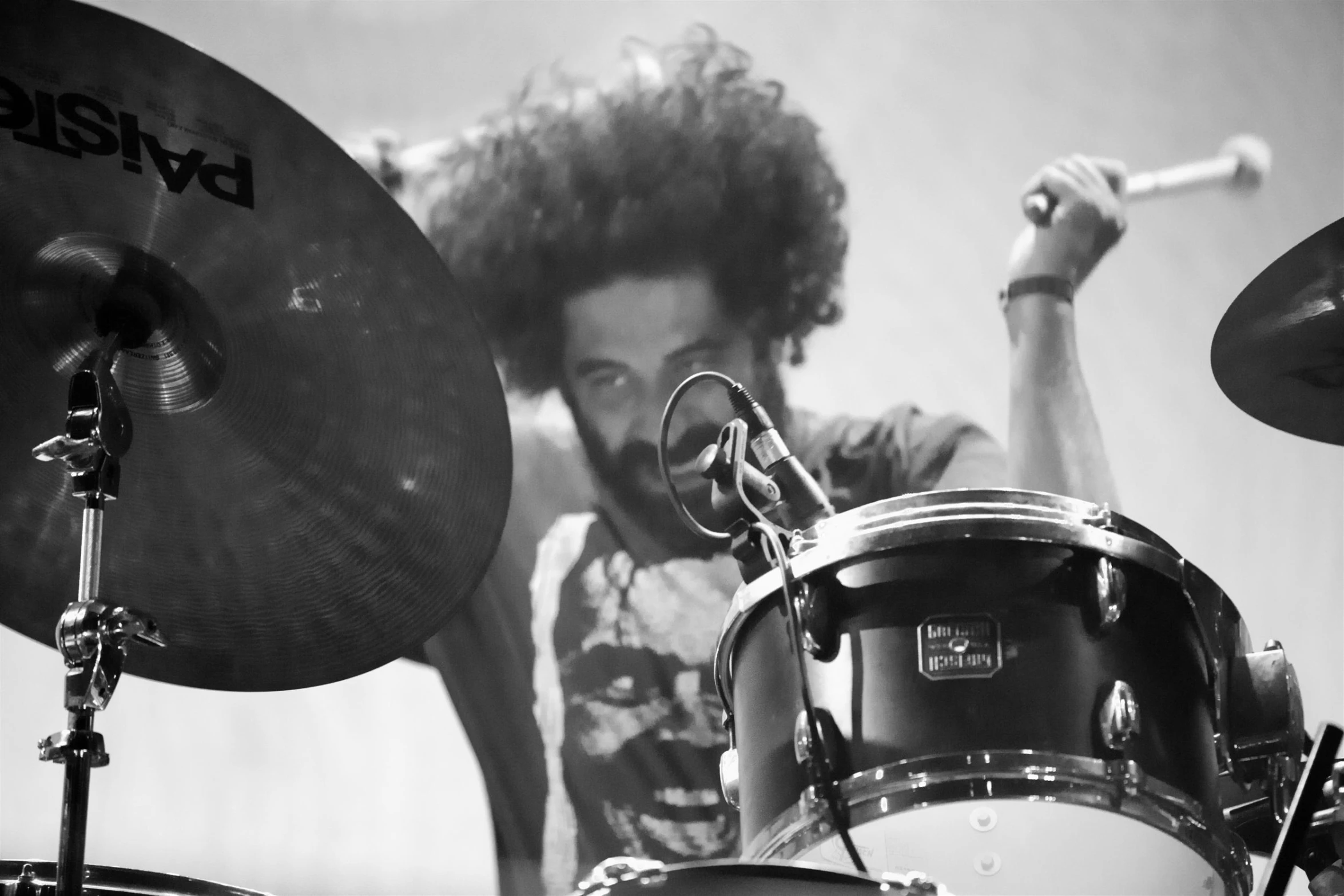 a guy with curly hair on a mic behind a drum set