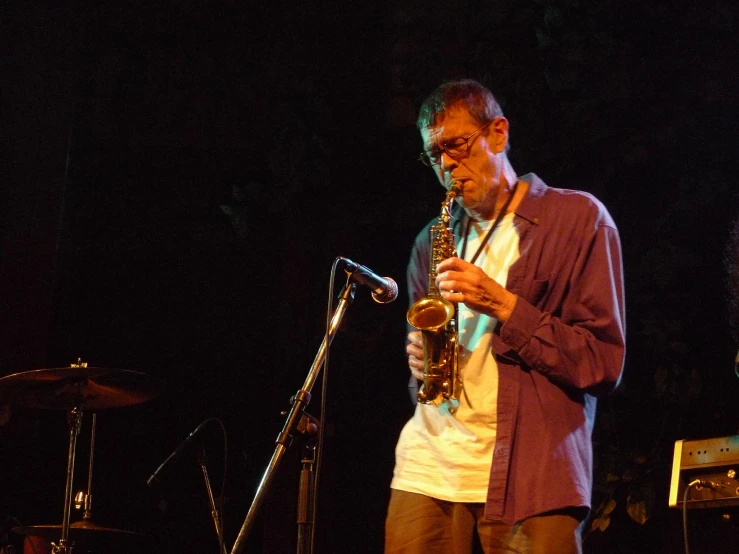 the man playing on the saxophone is standing next to a microphone and drums