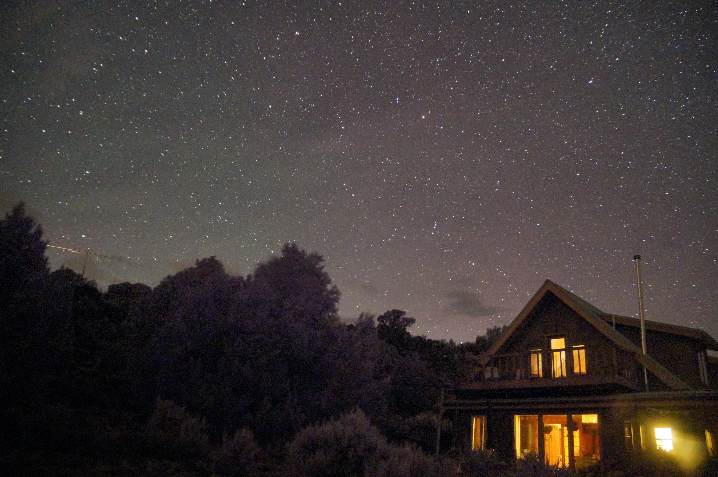 a house with some bright windows and trees and stars in the sky