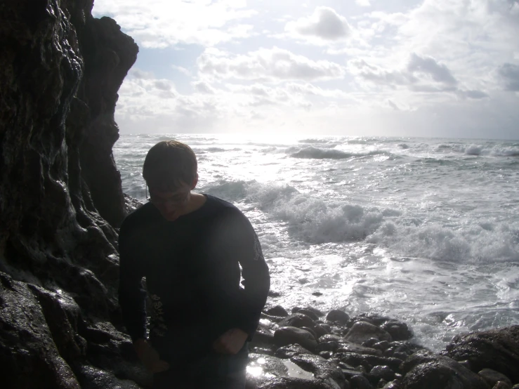 a man looks out over the water by the rocks