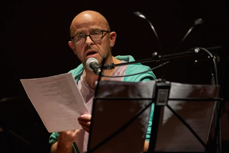 a man standing in front of a microphone and holding paper