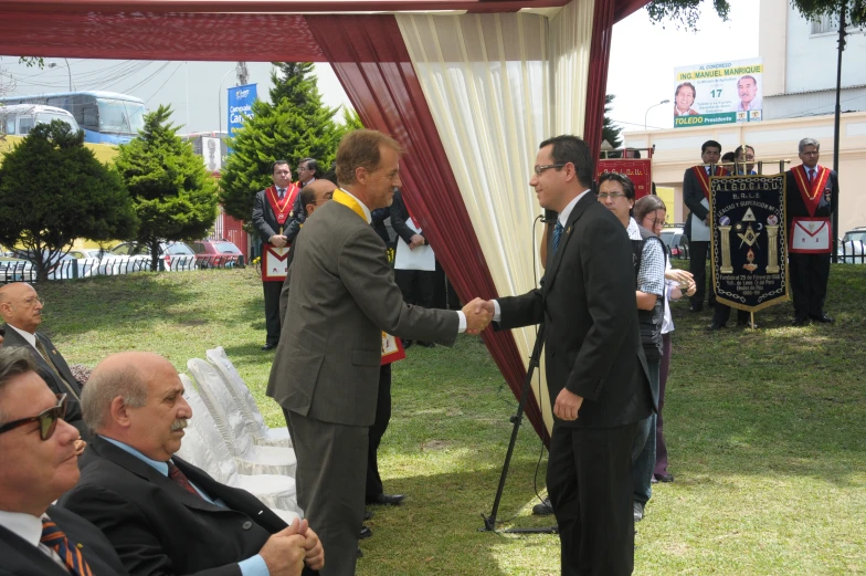 two men shaking hands with a flag behind them