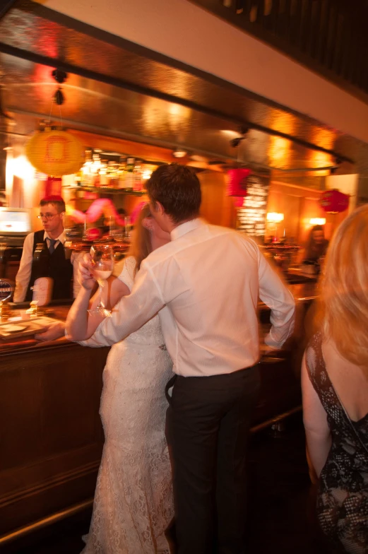 a man and woman dance with glasses of wine while others socialize at the bar