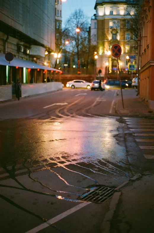 a wet street with cars and buildings lit up at night