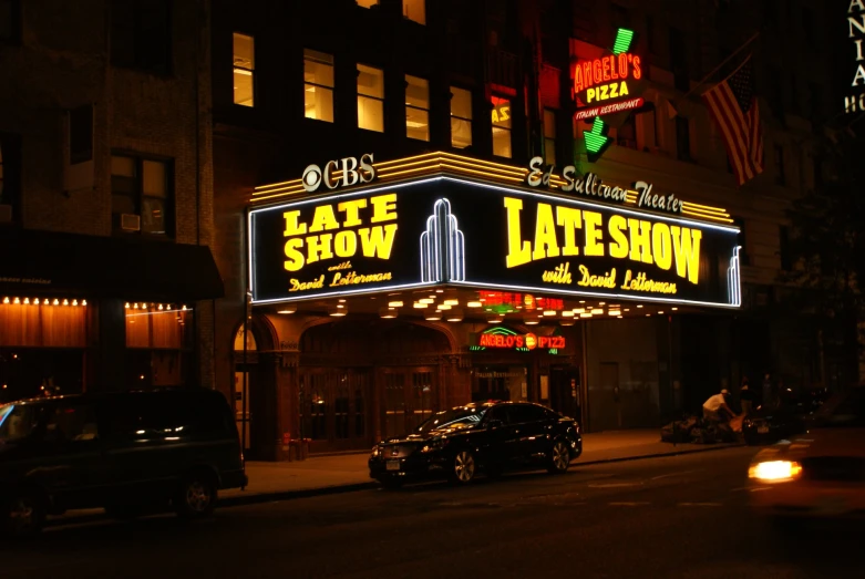 a city street at night with cars parked near the theater