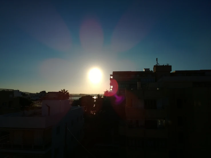 the sun shining through the blue sky near some buildings