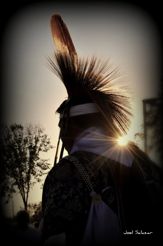 man in costume with feathers in front of sun