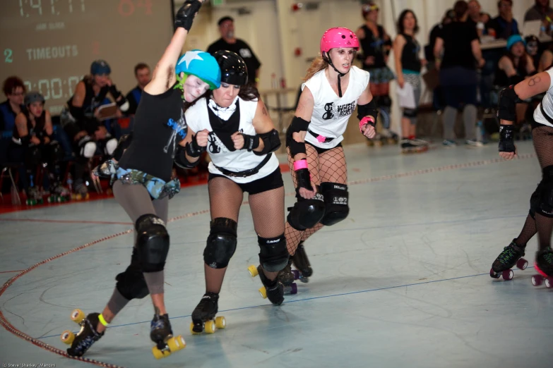 three young women rollerblading down a busy roller derby rink